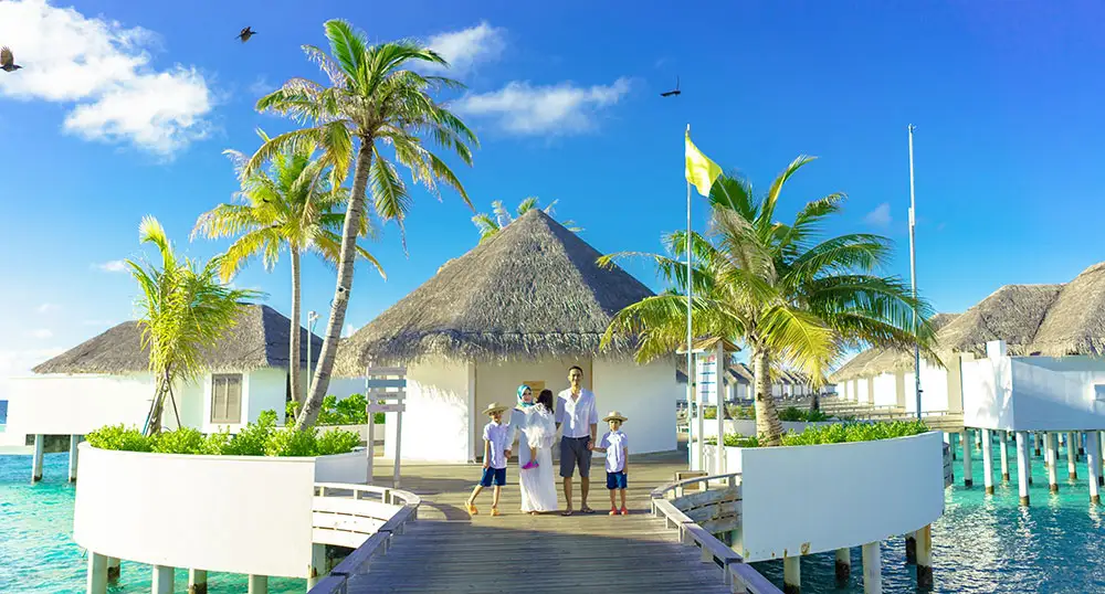 Family of four stands outside a tropical bungalow on the water