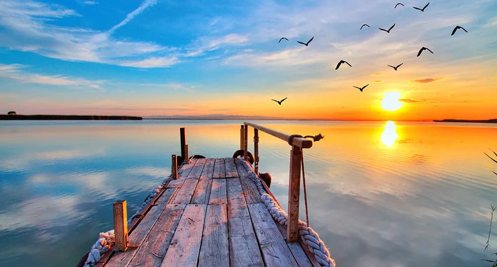 Wooden dock leading into large body of water, with a sunset