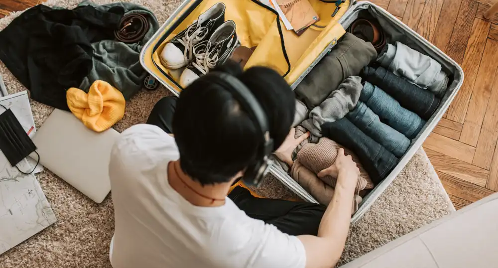 Man sits on the floor, wearing headphones and packing a suitcase for vacation