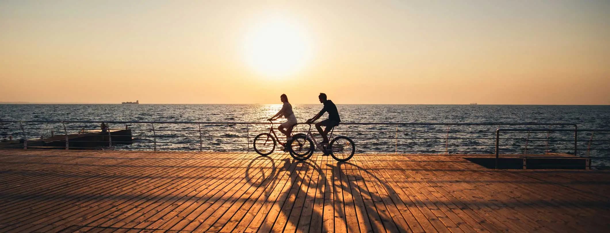 Two people ride bikes on a beach boardwalk