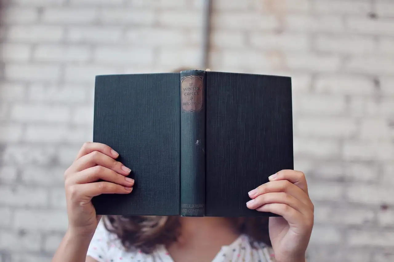 Woman hides her face behind a black-covered book