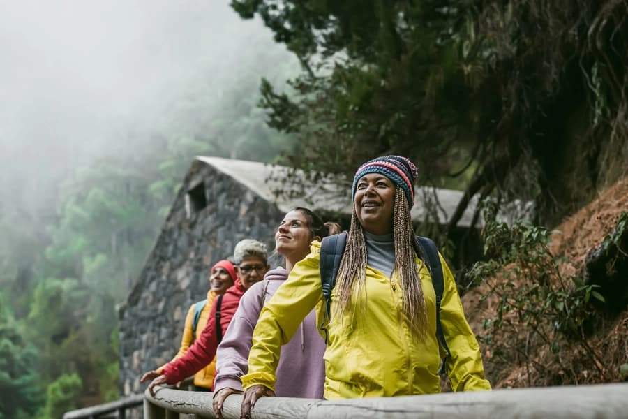 Four women grip a wooden rail as they hike through the rainforest