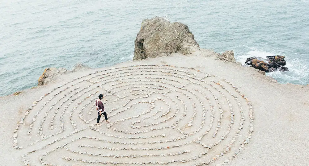 Woman walks through a simple rock maze on the beach