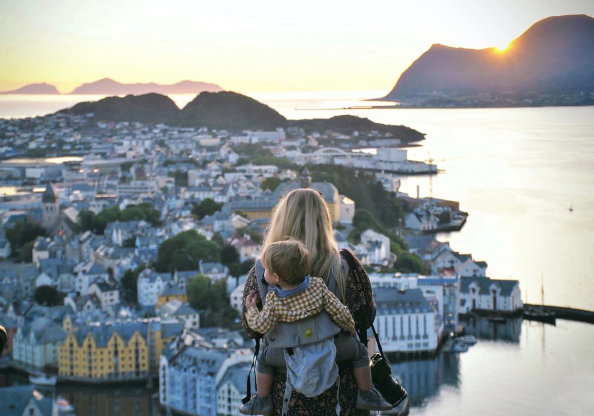 Woman with a baby on her back looks out over a scenic view of coastal Italy