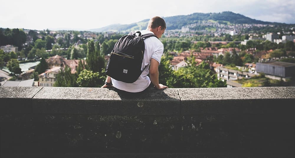 Young man sitting on a stone ledge, overlooking a mountain.