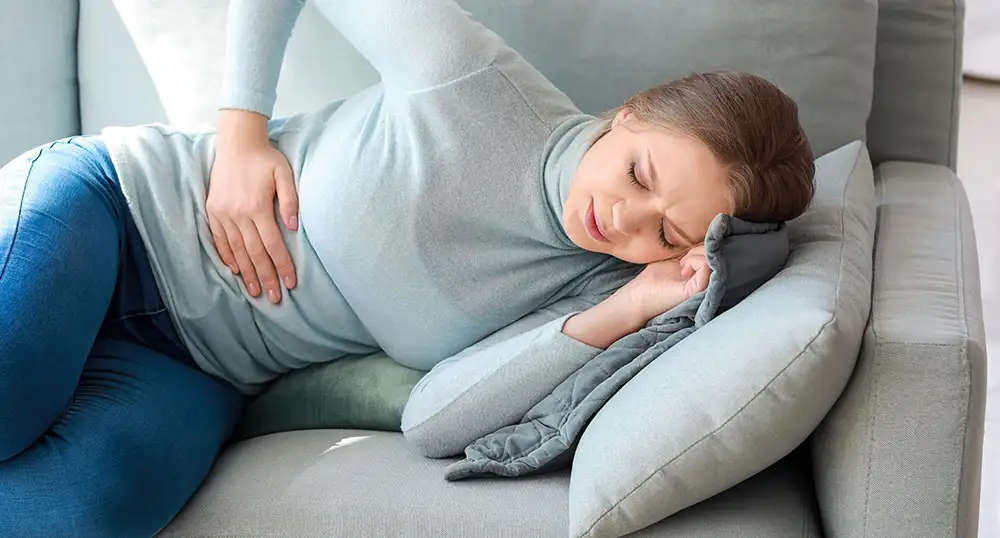 Woman lays on the couch, holding her side in pain