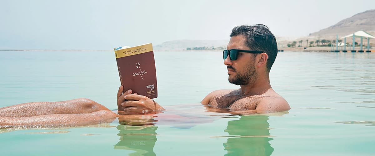 Man Wearing Sunglasses Reading Book in Ocean